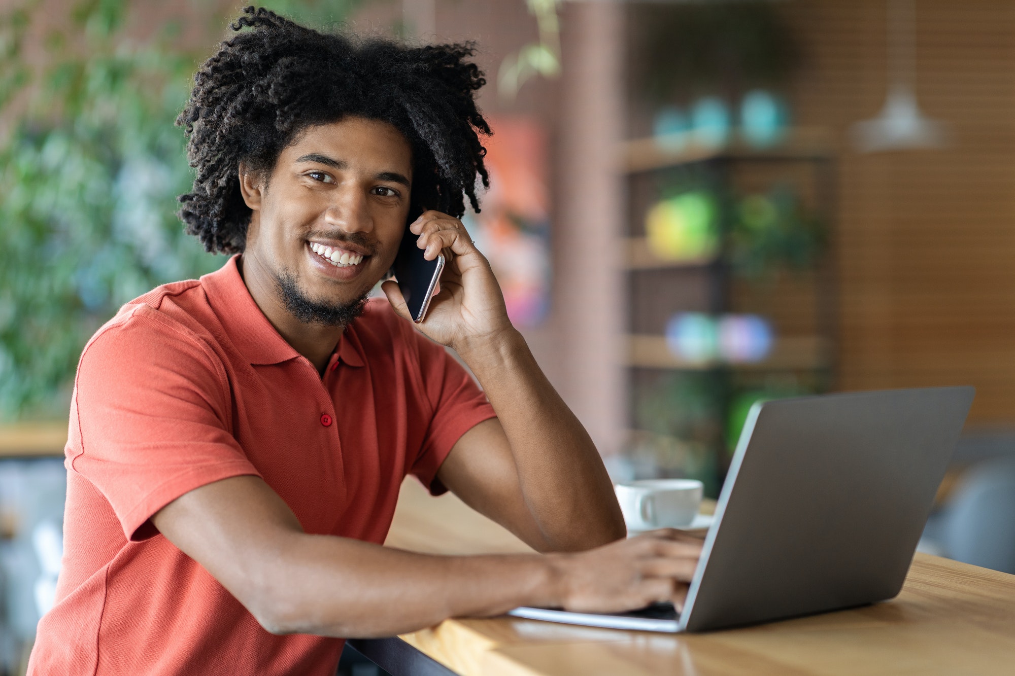 Modern Entrepreneur. Black Businessman Talking On Cellphone And Using Laptop In Cafe